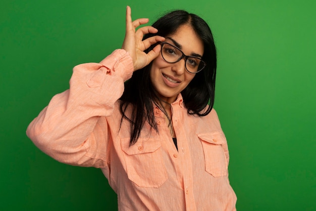 Foto gratuita hermosa joven sonriente con camiseta rosa y gafas aisladas en la pared verde