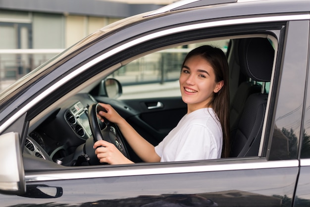 Hermosa joven sonriente conduciendo un coche en la carretera