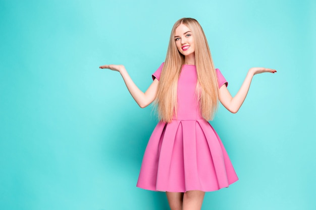 Hermosa joven sonriente en mini vestido rosa posando, presentando algo