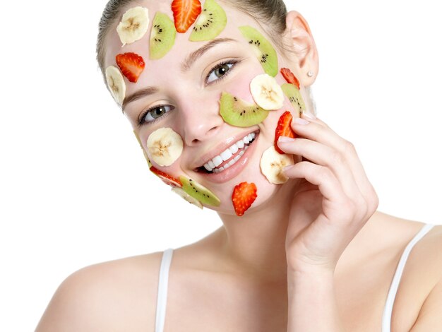 Hermosa joven sonriente mujer alegre con máscara de fruta en el rostro aislado en blanco