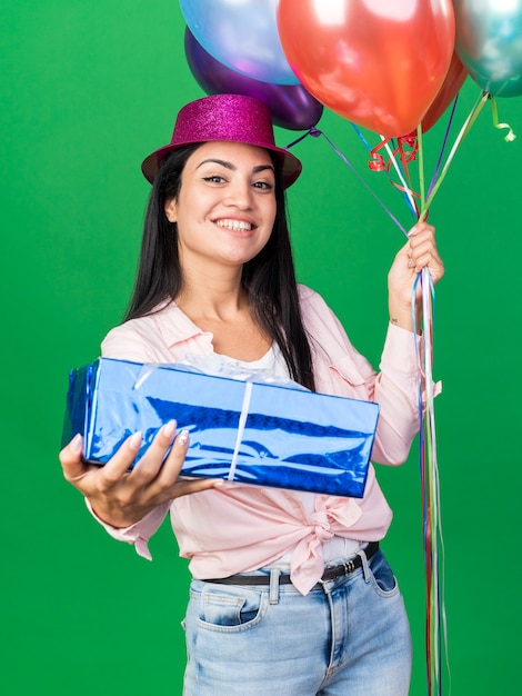 Hermosa joven sonriente con sombrero de fiesta sosteniendo globos con caja de regalo