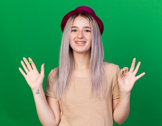 Hermosa joven sonriente vistiendo gorro de fiesta y tirantes extendiendo las manos