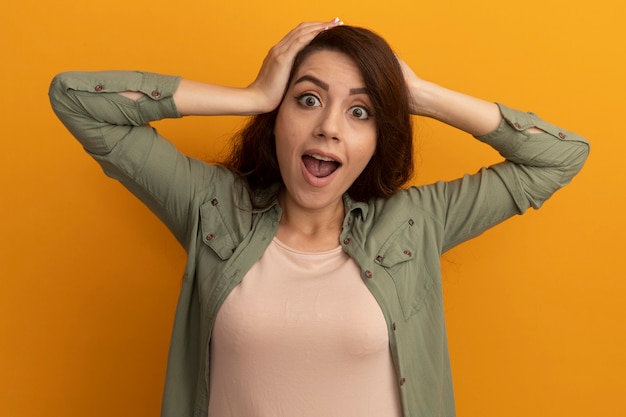 Foto gratuita hermosa joven sorprendida con camiseta verde oliva agarró la cabeza aislada en la pared amarilla