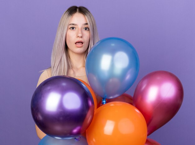 Hermosa joven sorprendida de pie detrás de globos