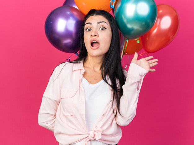 Hermosa joven sorprendida sosteniendo globos extendiendo la mano