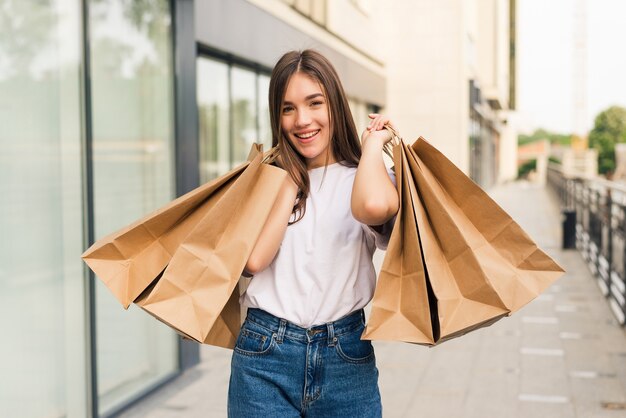 Hermosa joven sosteniendo bolsas de la compra y sonriendo al aire libre