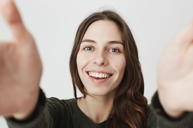 Hermosa joven sosteniendo la cámara con las manos estiradas, sonriendo tomando selfie