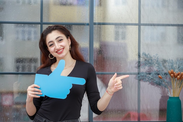 Hermosa joven sosteniendo un cartel con la mano y apuntándolo a un lado Foto de alta calidad