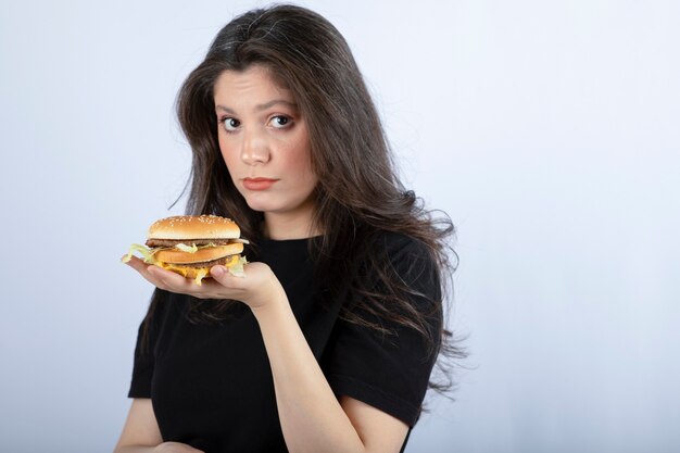 Hermosa joven sosteniendo una deliciosa hamburguesa de ternera.
