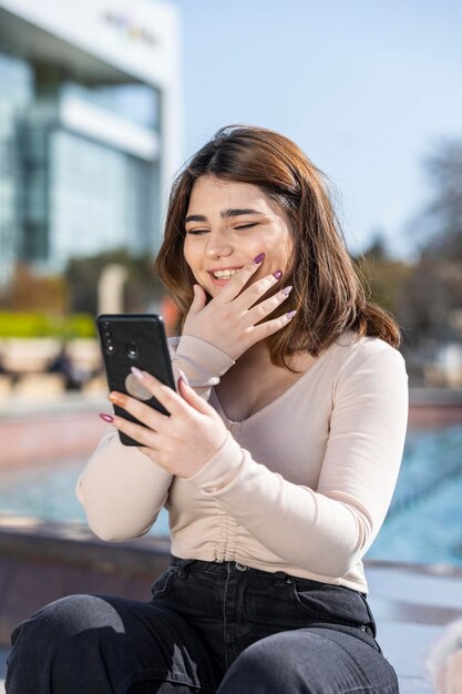 Hermosa joven sosteniendo su teléfono y sonriendo Foto de alta calidad