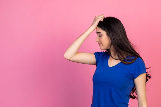 Hermosa joven sosteniendo sus manos en la cabeza y mirando hacia abajo sobre fondo rosa