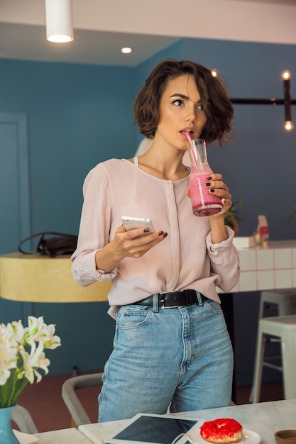 Hermosa joven sosteniendo teléfono móvil y beber batido