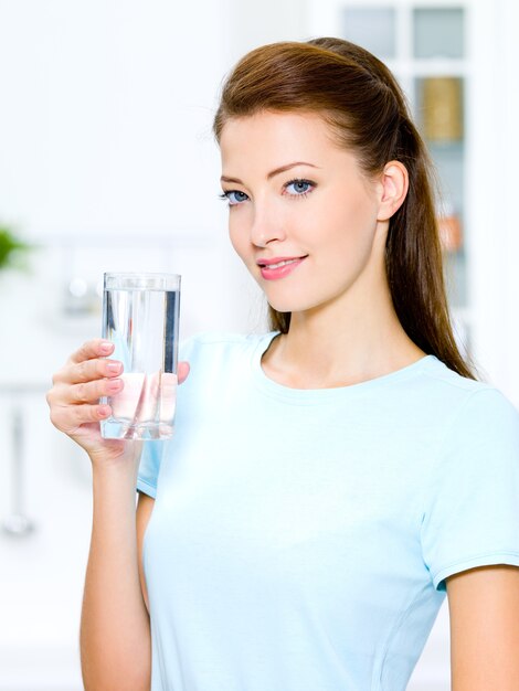 Hermosa joven sostiene un vaso con agua en la cocina