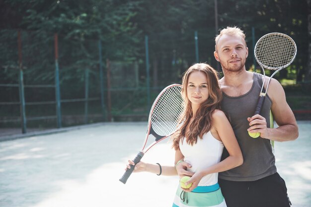 Una hermosa joven con su esposo pone en una cancha de tenis al aire libre.