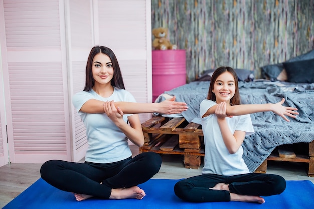 Hermosa joven y su hija deportiva están haciendo ejercicios sobre colchonetas