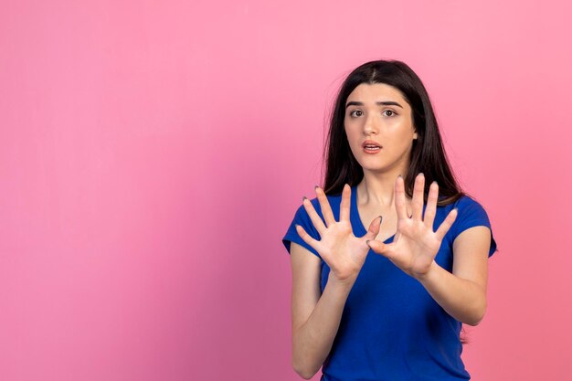 Una hermosa joven tiene miedo y los gestos se detienen en el fondo rosa Foto de alta calidad