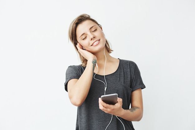 Hermosa joven tierna sonriente escuchando música en auriculares con los ojos cerrados.