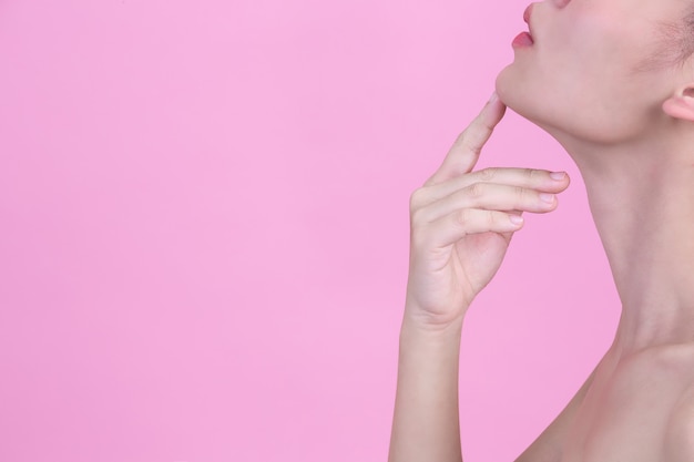 Hermosa joven toca su barbilla con su dedo índice en la pared de color rosa.