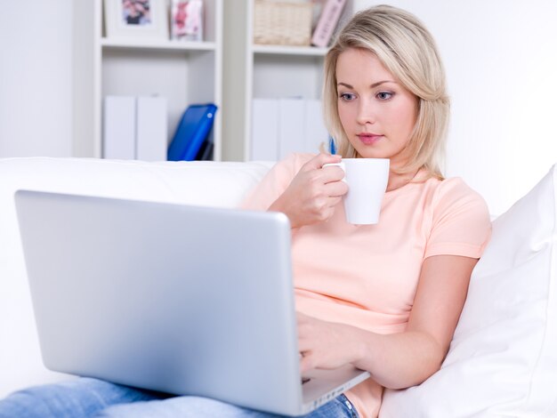 Hermosa joven tomando café y usando laptop