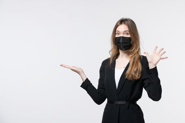 Hermosa joven en traje con mascarilla quirúrgica y apuntando algo mostrando cinco en blanco