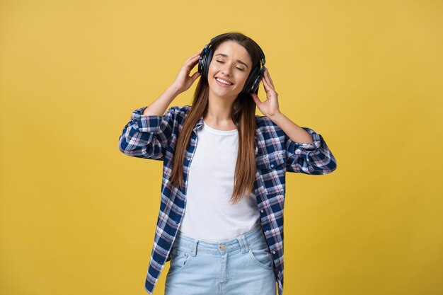 Hermosa joven tranquila escuchando la música en los auriculares con los ojos cerrados sobre fondo amarillo Primer plano