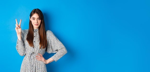 Hermosa joven vestida con cabello largo natural que muestra el número dos con los dedos y sonriente sta.