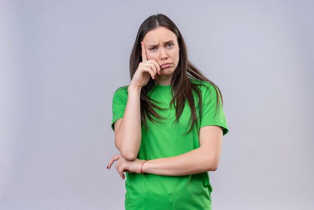 Hermosa joven vestida con camiseta verde mirando a la cámara cansado y aburrido esperando de pie sobre fondo blanco aislado