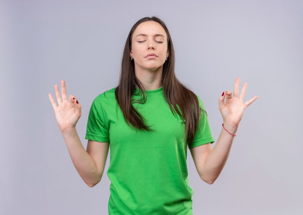 Hermosa joven vestida con camiseta verde relajante con los ojos cerrados haciendo gesto de meditación con los dedos de pie sobre fondo blanco aislado