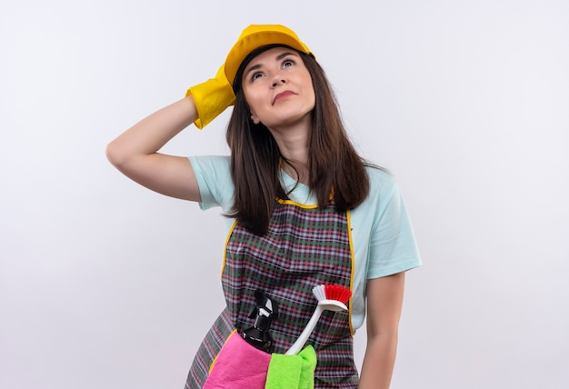 Hermosa joven vestida con delantal, gorra y guantes de goma mirando hacia arriba con mirada de ensueño