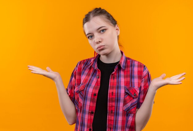 Hermosa joven vistiendo camisa roja extiende las manos sobre la pared amarilla aislada