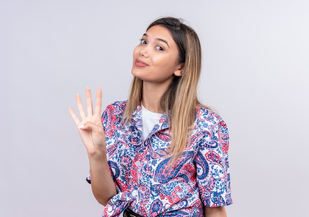 Foto gratuita una hermosa joven vistiendo una camiseta estampada de paisley que muestra el número cuatro con los dedos mientras mira en una pared blanca