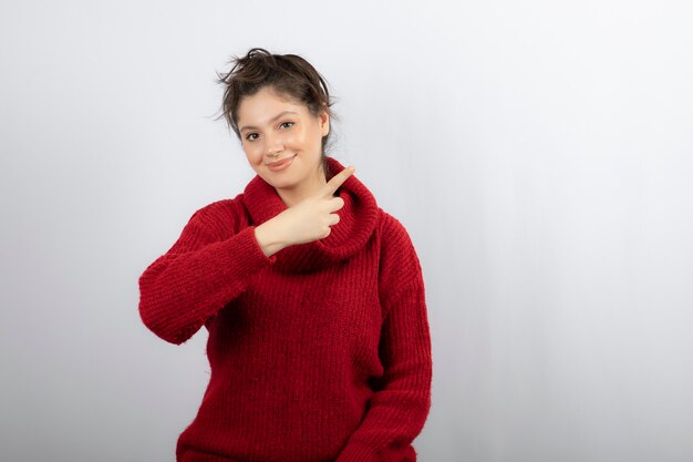 Hermosa joven vistiendo suéter y apuntando con el dedo hacia un lado.