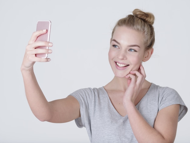 Hermosa jovencita caucásica hace autorretratos. Feliz mujer maravillosa con teléfono celular móvil en manos