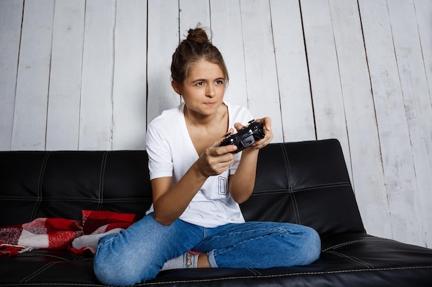 Hermosa jovencita jugando videojuegos, sentada en el sofá en casa. copie el espacio.