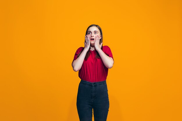 Hermosa jovencita mirando sorprendido aislado en naranja