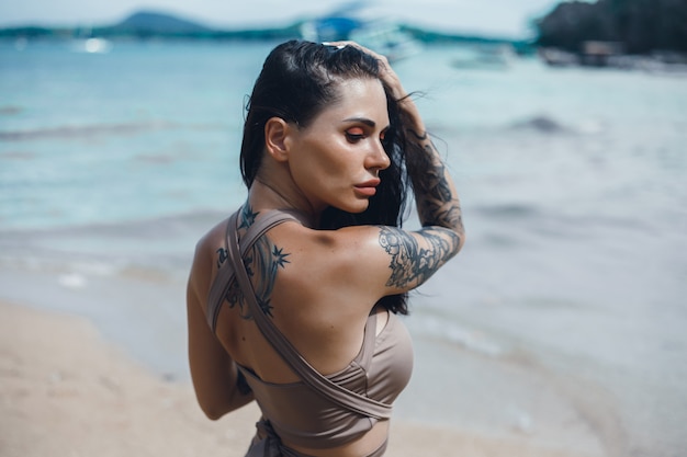 Hermosa jovencita posando en la playa, el océano, las olas, el sol brillante y la piel bronceada.