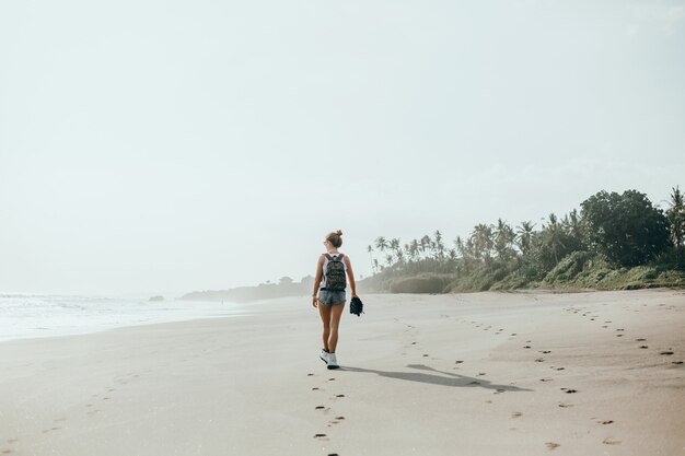 Hermosa jovencita posando en la playa, el océano, las olas, el sol brillante y la piel bronceada.