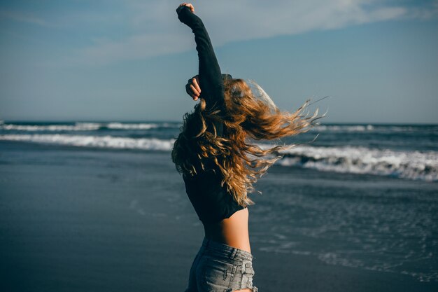 Hermosa jovencita posando en la playa, el océano, las olas, el sol brillante y la piel bronceada.