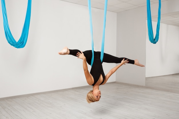 Hermosa jovencita practicando yoga aéreo en el gimnasio.