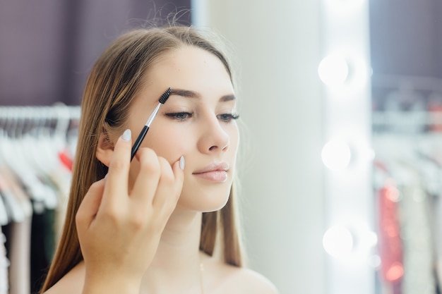 Hermosa jovencita rubia hace un maquillaje natural frente al espejo