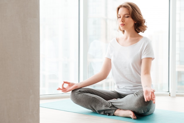 Hermosa jovencita sentada junto a la ventana hacer ejercicios de yoga.