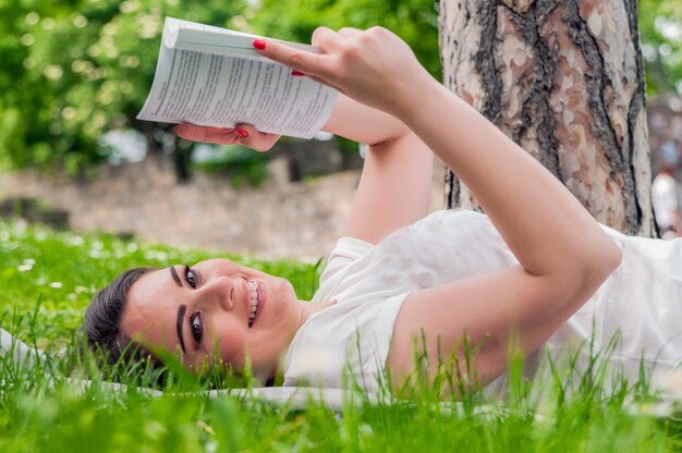 Hermosa lectura morena joven en un prado en el parque