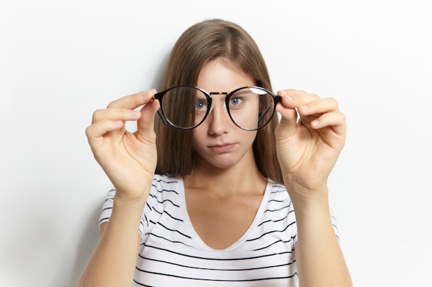 Hermosa linda chica teeage miope en elegante camiseta a rayas poniéndose sus primeros anteojos. Concepto de corrección de la visión, óptica, miopía y miopía. Enfoque selectivo en gafas