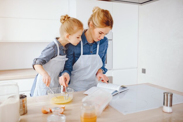 hermosa madre con una camisa azul y un delantal está preparando la cena en casa en la cocina