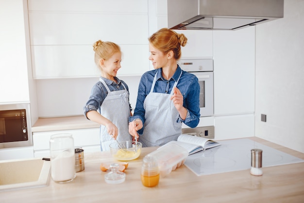 hermosa madre con una camisa azul y un delantal está preparando la cena en casa en la cocina