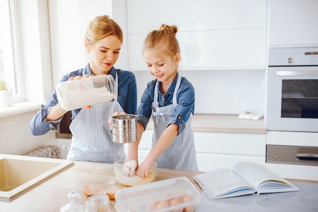 hermosa madre con una camisa azul y un delantal está preparando la cena en casa en la cocina