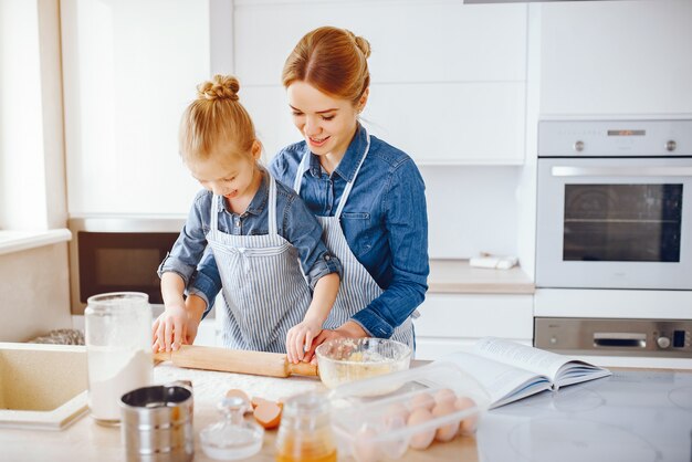 hermosa madre con una camisa azul y un delantal está preparando la cena en casa en la cocina