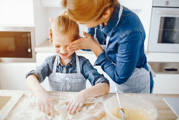 hermosa madre con una camisa azul y un delantal está preparando la cena en casa en la cocina