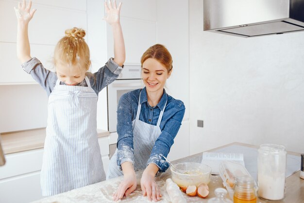 hermosa madre con una camisa azul y un delantal está preparando la cena en casa en la cocina