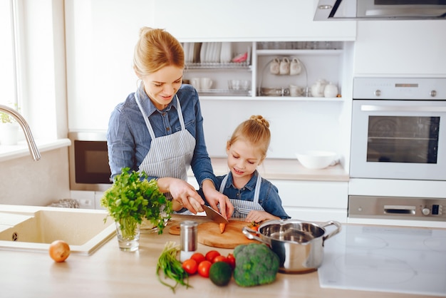 hermosa madre con una camisa azul y un delantal está preparando una ensalada de vegetales frescos en casa